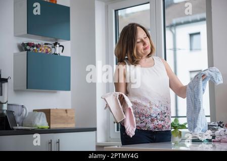 Schwangere Frau faltet Babykleidung in der Küche, München, Bayern, Deutschland Stockfoto