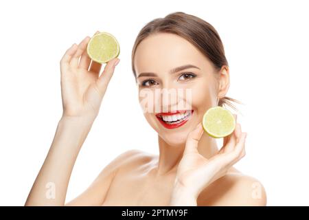 Ein hübsches Mädchen hält zwei Hälften frische Limette in beiden Händen und sieht gerade aus. Lächelmodell mit gesunder Haut. Stockfoto