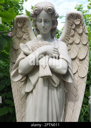 Ein Engel mit einer Taube. Skulptur auf dem Friedhof. Die Gestalt eines Engels mit Flügeln, der einen Vogel in den Armen hält. Klagen für den Verstorbenen. Grabstein Stockfoto