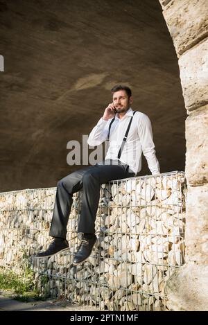 Geschäftsmann, der mit dem Handy sitzt und spricht, München, Bayern, Deutschland Stockfoto