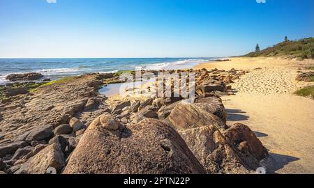 Vulkanisches Felsenregal mit einem Felsenbecken in Point Arkwright, Coolum, Sunshine Coast, Queensland. Blick nach Süden entlang des Sandstrands. Stockfoto