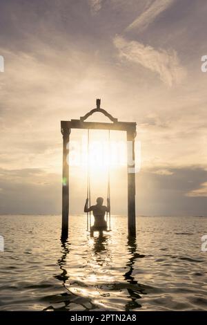 Rückansicht einer Frau, die auf einer Seilschaukel am Strand gegen Sonnenuntergang sitzt, Gili Trawangan, Lombok, Indonesien Stockfoto