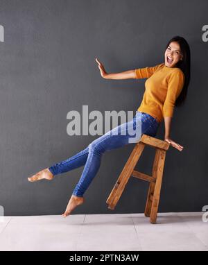 Sie ist über dem Mond. Porträt einer glücklichen jungen Frau, die sich auf einen Hocker lehnt Stockfoto