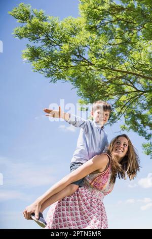 Fröhlicher Junge, der Huckepackfahrt auf der Mutter beim Picknick in Bayern genießt Stockfoto