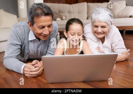 Erstellen eines Social-Media-Profils für Oma und Opa. Ein junges Mädchen und ihre Großeltern liegen auf dem Boden und schauen auf einen Laptop Stockfoto