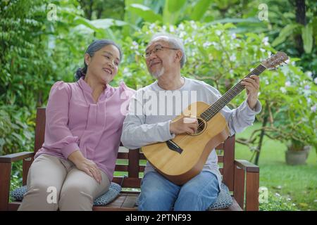 Glückliches asiatisches Seniorenpaar älterer Mann, der Gitarre spielt, während seine Frau zu Hause im Freien zusammen singt, Aktivität, Familiengesundheit, Lebensstil genießen Stockfoto