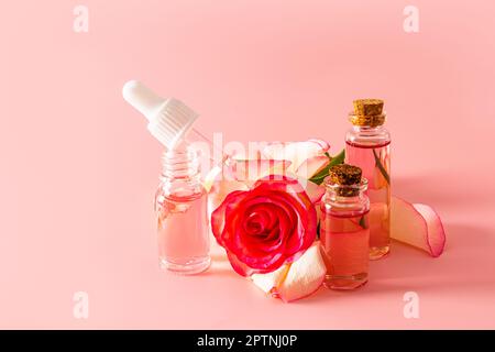 Eine offene Flasche Rosenöl und eine ölgefüllte Pipette, Rosenwasser in Glasflaschen mit einem Stopfen auf dem Hintergrund einer Rosenblume. Natürliche Pflege Stockfoto