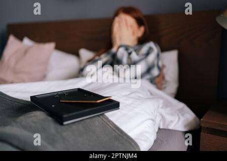 Nahaufnahme selektiver Fokussierung des Bilderrahmens auf verschwommener Rückwand einer weinenden, trauernden jungen Frau, die auf dem Bett liegt und das Gesicht mit der Hand bedeckt. Stockfoto