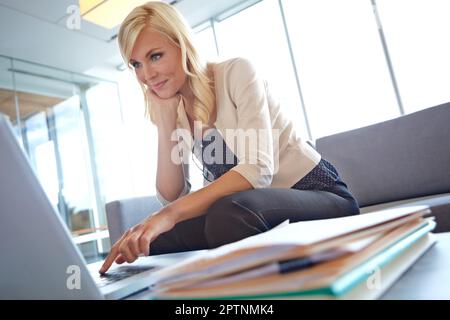 Forschung ist der Schlüssel zu einer guten Präsentation. Eine wunderschöne blonde Frau, die im Büro an ihrem Laptop arbeitet. Stockfoto
