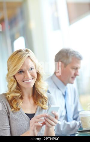 Sie ist immer in Kontakt – Smartphone-Technologie. Eine attraktive Geschäftsfrau, die ihr Smartphone während eines Geschäftstreffens verwendet. Stockfoto