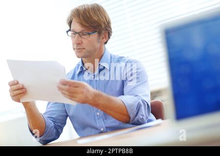 Ein Geschäftsdokument lesen. Reifer, intelligenter Geschäftsmann in einem Büro, der sich auf ein wichtiges Geschäftsdokument konzentriert. Stockfoto