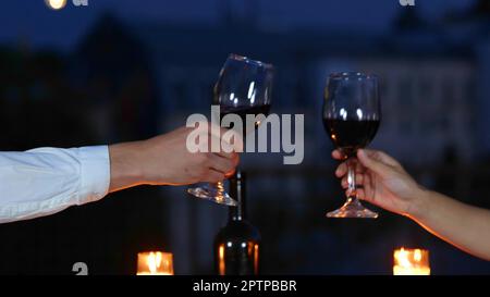 Nahaufnahme eines jungen, kaukasischen glücklichen Paares, das seinen Jahrestag bei einem romantischen Date am Abend auf dem Dach feiert. Ein schöner Mann und eine schöne Frau, die gutes Rot trinken Stockfoto