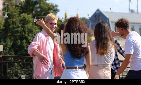 Fröhliche Leute treffen sich draußen in der Stadt und haben gute Laune auf einer Party. Fröhliche, weiße, junge, männliche und weibliche Freunde versammelten sich auf einer Party auf dem Dach Stockfoto