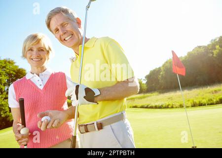 Golf hält uns regelmäßig zusammen. Ältere Ehepaare halten ihre Golfschläger und Bälle auf dem Grün. Stockfoto