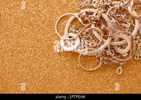 Viele teure goldene Schmuckringe, Ohrringe und Halsketten auf goldenem Glitzerhintergrund mit glänzenden Funkeln. Pfandhaus oder Schmuckgeschäft Konzept Stockfoto