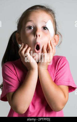 Nahaufnahme lustiges, bezauberndes, dunkelhaariges kleines Mädchen mit Verletzung und Fleck im Gesicht, tragen Sie ein rosa Hemd auf weißem Hintergrund. Angst vor Elternreaktionen. Rz Stockfoto