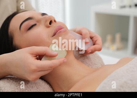 Junge Frau, die im Schönheitssalon eine Gesichtsmassage mit Gua-sha-Werkzeugen erhält Stockfoto