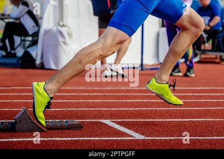 Nahaufnahmen männlicher Athleten beginnen in Startblöcken, Sprintrennen, Sommersportmeisterschaften und leuchtend gelben Spikes-Schuhen Stockfoto