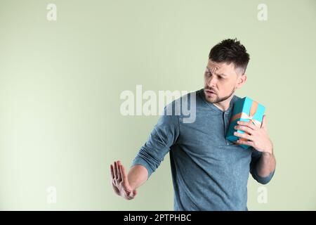 Gieriger Mann, der eine Geschenkbox auf hellem Hintergrund versteckt, Platz für Text Stockfoto