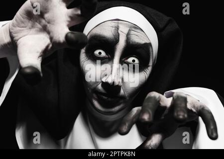 Gruselige, teuflische Nonne, die vor schwarzem Hintergrund Angst hat. Halloween-Party-Look Stockfoto