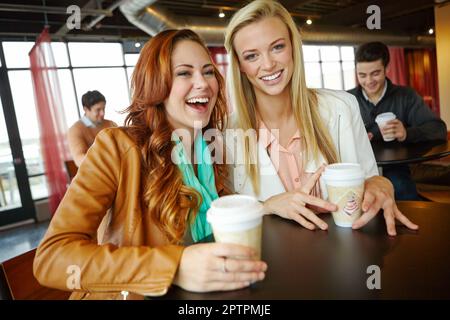 Kichern und alte Zeiten aufholen. Zwei attraktive junge Freundinnen, die zusammen eine Tasse Kaffee trinken. Stockfoto