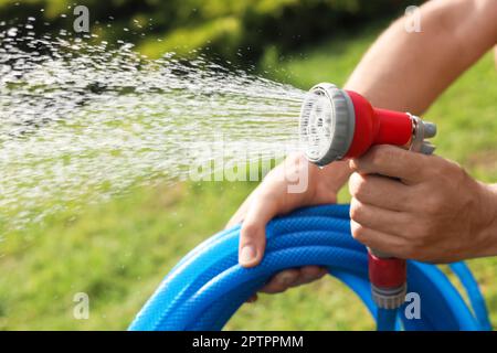 Mann, der Wasser aus dem Schlauch spritzt, im Garten, Nahaufnahme Stockfoto