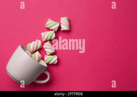 Umgekehrte Tasse mit köstlichen bunten Marshmallows auf purpurfarbenem Hintergrund, flach liegend. Platz für Text Stockfoto