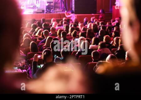 Die Zuschauer sitzen im Flur und sehen sich ein Konzert an. Die Leute im Auditorium schauen sich die Vorstellung an. Theaterpublikum. Musikkonzert oder -Festival. Aus Stockfoto