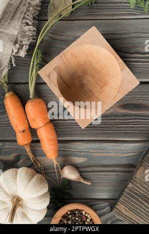 Reife ungeschälte Orangenkarotte mit grünem Transport. Leere Schüssel auf dem Küchentisch aus Holz. Flache Lay-Ansicht. Anordnung von frischem Gemüse und Aromen. Fertig machen Stockfoto