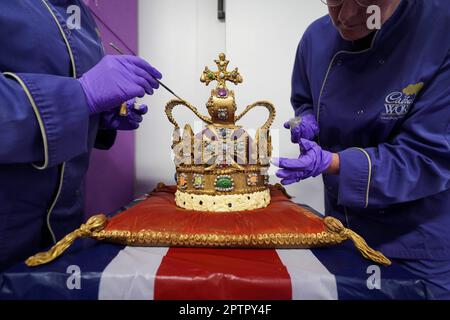 Die Cadbury World Chocolatiers Dawn Jenks und Donna Oluban verleihen der Cadbury World in Birmingham, einer 45cm m hohen Schokoladenreproduktion der St. Edward's Crown, den letzten Schliff. Es dauerte zwei Tage, um ihre Version der Krone zu bauen, die bei der Krönung von König Karl III. Mit weißer Schokolade und Milchschokolade verwendet und mit essbarem Glitzer bestaubt wird. Bilddatum: Mittwoch, 26. April 2023. Stockfoto