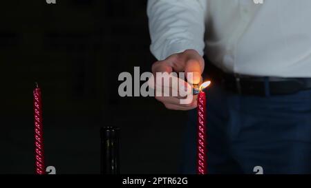 Nahaufnahme eines jungen Mannes, der Kerzen auf dem Tisch im Freien bei einem romantischen Date am Abend zündet und ein romantisches Abendessen mit Essen und Rotwein zubereitet. Vorschlag Stockfoto