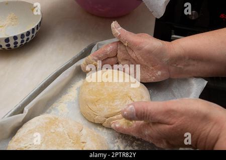 Der Prozess der Zubereitung von süßem Brotteig zu Hause. Nahaufnahme von Frauenhänden, die die Brötchen mit Mehl auf einem Tablett zubereiten, bevor sie in den Ofen gehen Stockfoto