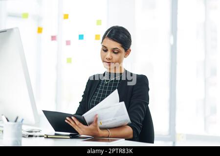 Ich sehe mir ein paar Geschäftsberichte an. Eine junge Geschäftsfrau, die eine Akte in einem Büro durchsucht. Stockfoto