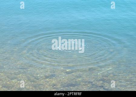 Runde Wassertropfen über den Kreisen auf dem Wasser. Wassertropfen, Wirbeln und Spritzen. Wellen auf dem Hintergrund des Meerestextur-Musters. Stockfoto
