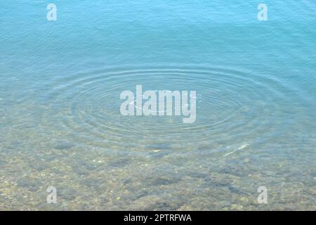 Runde Wassertropfen über den Kreisen auf dem Wasser. Wassertropfen, Wirbeln und Spritzen. Wellen auf dem Hintergrund des Meerestextur-Musters. Stockfoto