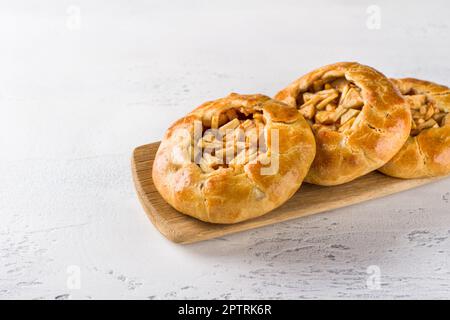 Süße Mini-Pasteten mit Äpfeln und Zimt auf einem Holzbrett mit einer Serviette auf hellgrauem Hintergrund. Köstliches hausgemachtes Essen Stockfoto