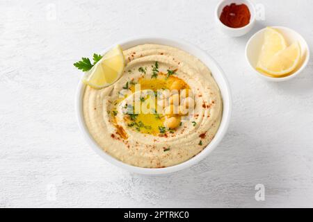 Traditioneller Hummus mit Kichererbsen, Petersilie, Gewürzen und Zitronenkeil in einer weißen Schüssel auf hellgrauem Hintergrund, Draufsicht. Köstlich hausgemacht Stockfoto