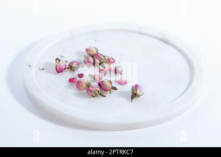 Schöne und rosafarbene kleine getrocknete Rosen auf weißem Hintergrund mit Marmorplatte Stockfoto