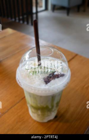 Grüner Eistee mit Milch in einem Plastikbecher auf einem Holztisch, Stockfoto Stockfoto