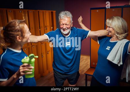 Sportteam aus Senioren und jungen Frauen, die sich in der Umkleide wohlfühlen und gemeinsam Freude haben Mann aufgeregte und jubelnde Frauen. Stockfoto
