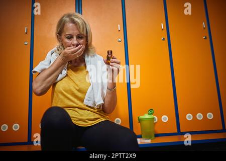 Seniorin in Sportbekleidung, die nach dem Training Medikamente und Vitamine einnimmt. Gesundheit, Lebensstil, Seniorenleben-Konzept. Stockfoto