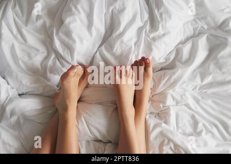 Aufnahmen aus dem hohen Winkel von zwei unbekannten Frauenfüßen, die sich zu Hause auf dem Bett entspannen. Stockfoto