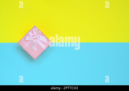 Kleine rosa Geschenkkarton liegen auf Textur Hintergrund der Mode pastell-blaue und gelbe Farben Papier in minimalen Begriff. Stockfoto