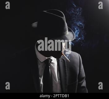 Afroamerikanischer Mann posiert vor schwarzem Hintergrund. Vintage-Hitman in der Mafia sieht beim Rauchen einer Zigarette gefährlich und kantig aus. Modisch Stockfoto