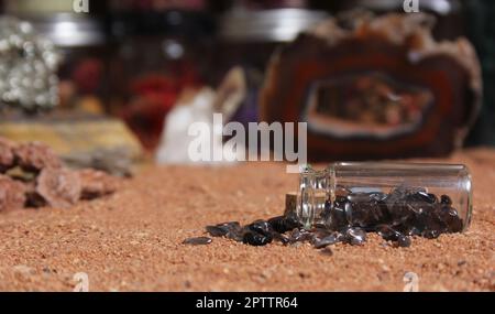 Flasche Chakra-Steine auf rotem Sand mit agatisierter Koralle im Hintergrund mit flachem Innengewinde Stockfoto