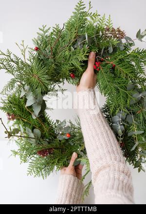 Stilvoller Weihnachtskranz für den Innenraum, hängen Sie den Kranz an die Tür. Handgemacht, hält das Mädchen einen frisch gemachten Kranz in der Hand. Die Atmosphäre von Stockfoto