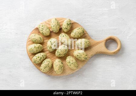 Gnocchi aus rohem Käse oder Teigtaschen mit Kräutern auf einem Holzbrett auf hellgrauem Hintergrund, Draufsicht. Köstliche hausgemachte vegetarische Speisen Stockfoto