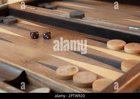 Braune Backgammon-Würfel und -Stücke auf Holzbrett Stockfoto