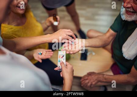 Gesichtslose Aufnahme von Seniorinnen und Senioren, die im Umkleideraum sitzen und Tabletten nehmen. Gesundheit, Lebensstil, Seniorenleben-Konzept. Stockfoto