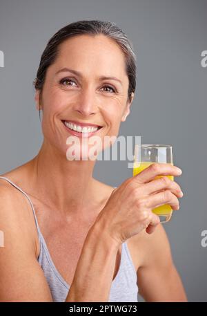 Vitamin-C.-Studioporträt einer attraktiven, reifen Frau, die ein Glas Orangensaft trinkt Stockfoto